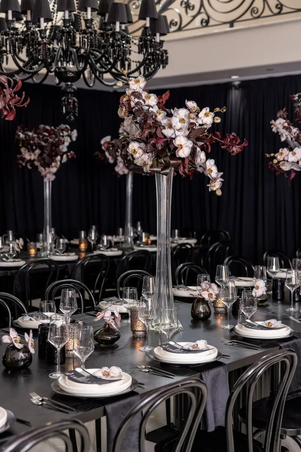 Dark, moody orchid and foliage centerpiece designed by a party planner under a black beaded chandelier