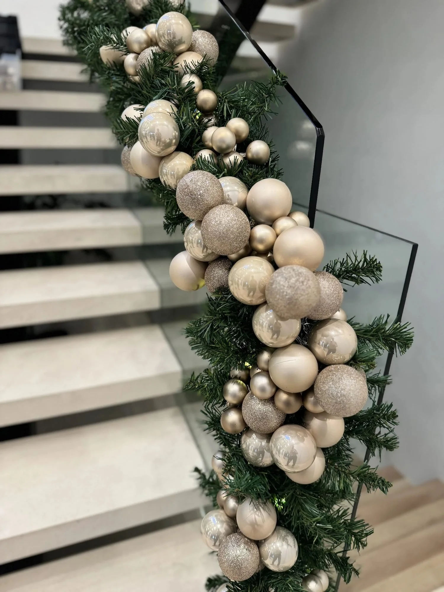 Staircase garland installation with champagne and gold ornaments on a glass railing, by Eddie Zaratsian in Los Angeles