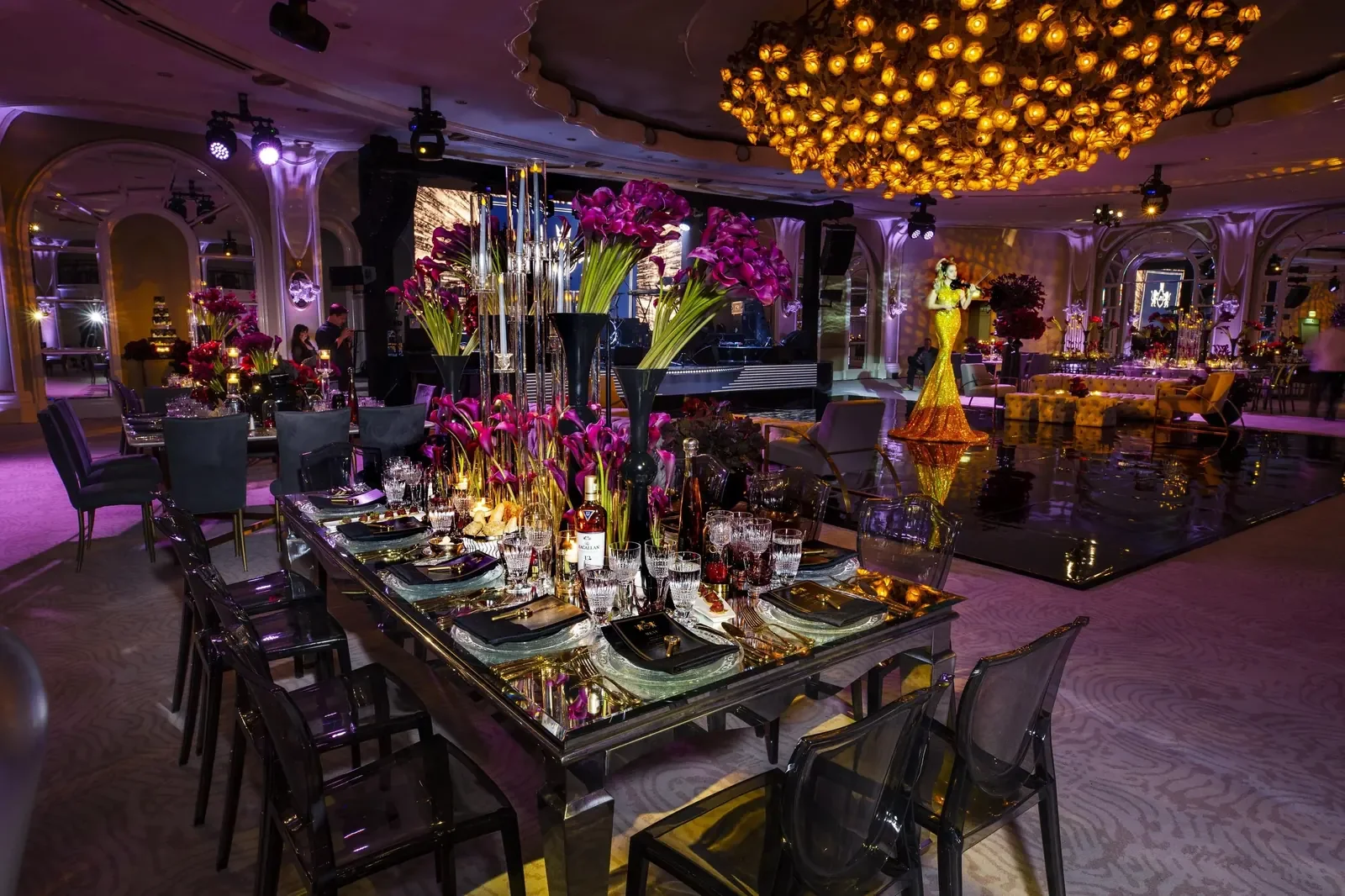 Violinist performing in a gold gown beneath a gold flower chandelier at a birthday celebration produced by a party planner