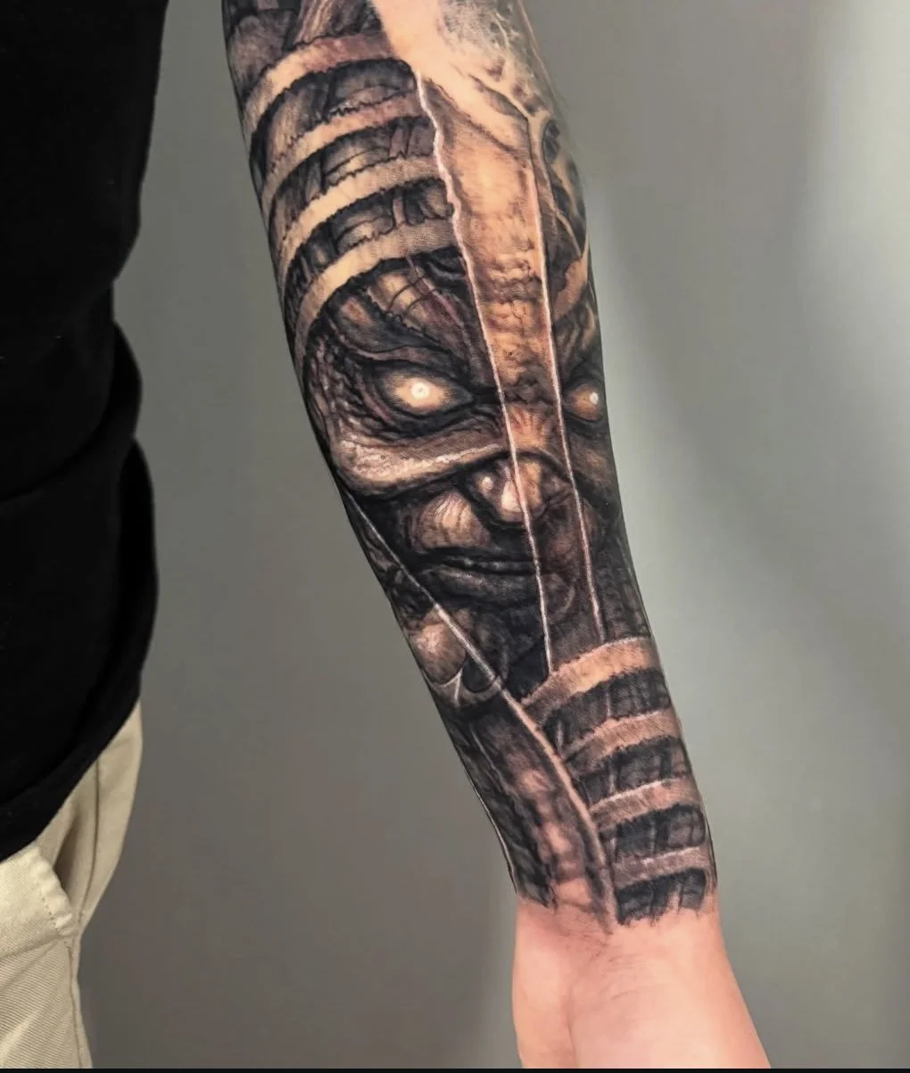 Tattoo of a tribal warrior or tribal mask on a person's forearm, with detailed shading and patterns.