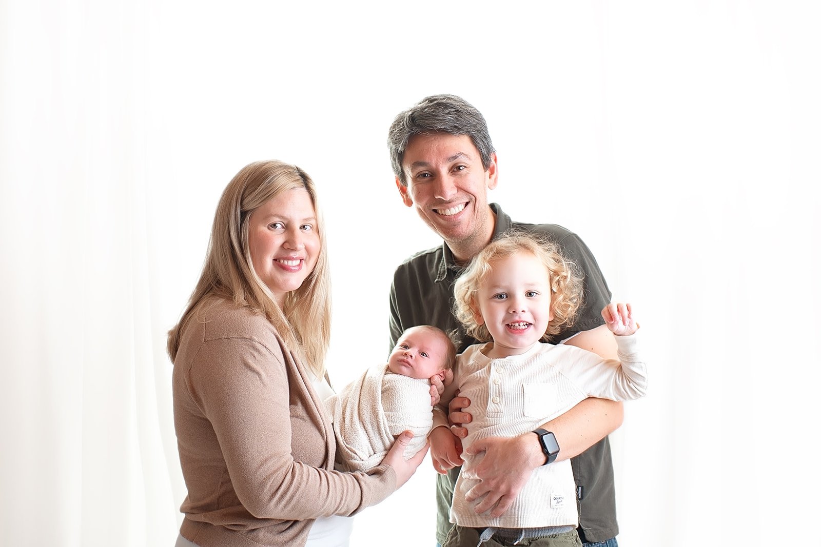 family with newborn baby boy smiling in front of a white background in studio in Monroe, NC
