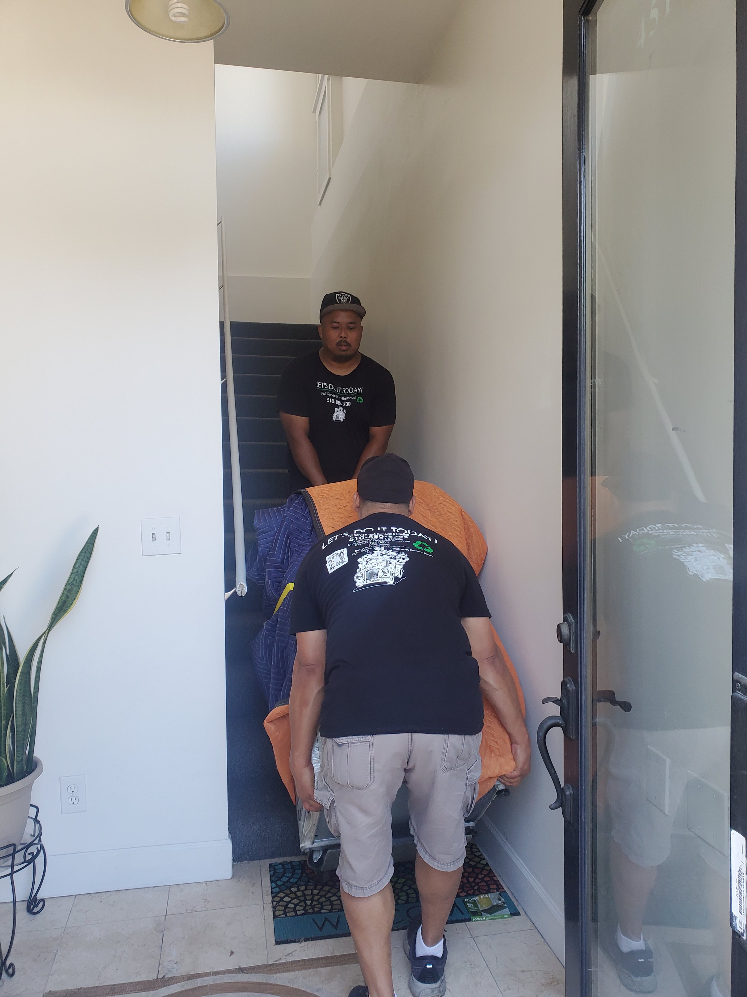 Let's Do It Today crew carrying a couch down a stairwell during a junk removal job