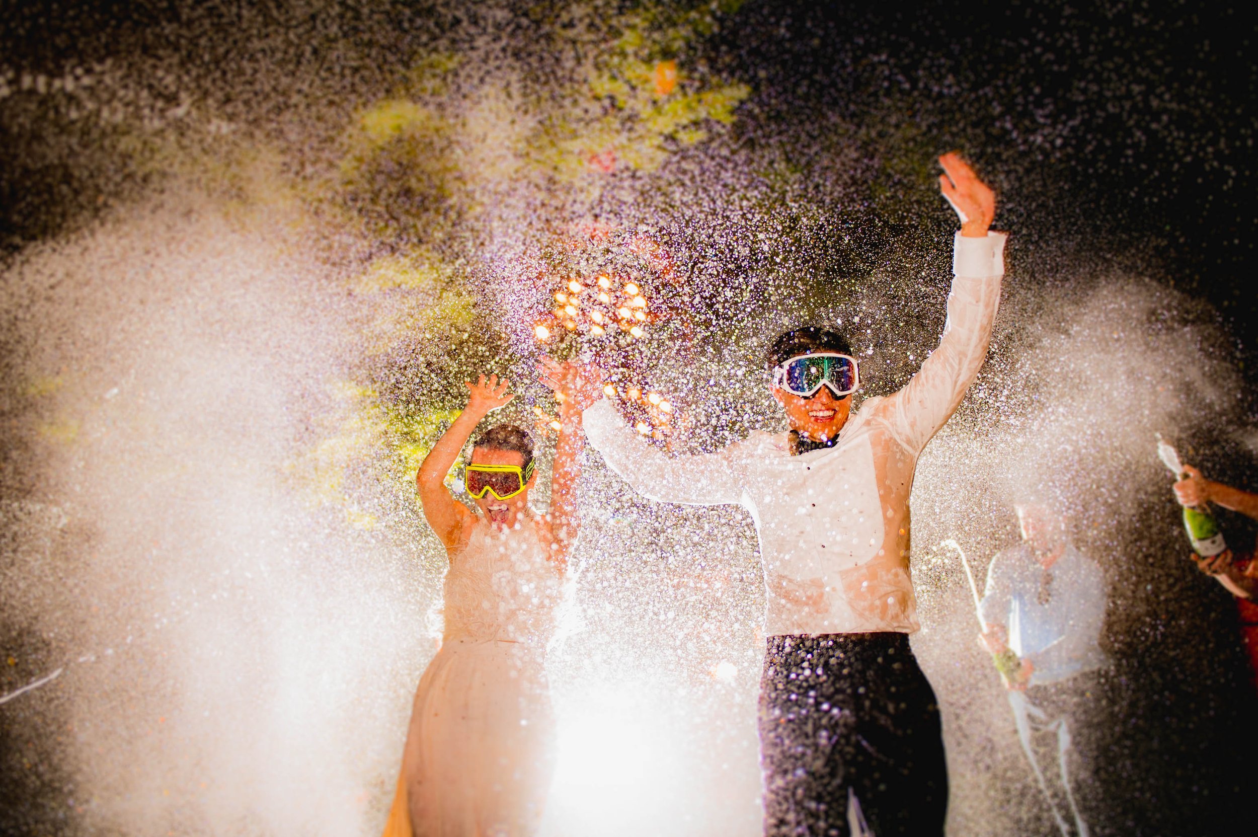 the bride and groom run through sprayed champagne as they wear ski goggle and are soaked