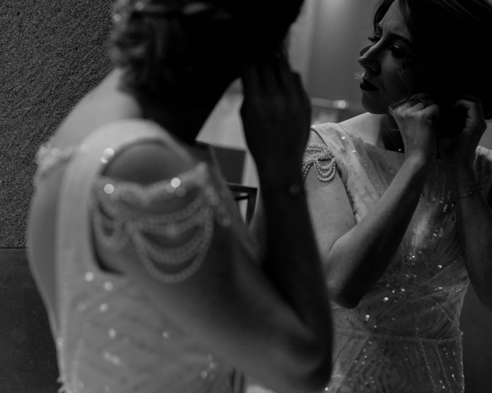 bride puts on her earrings in the mirror