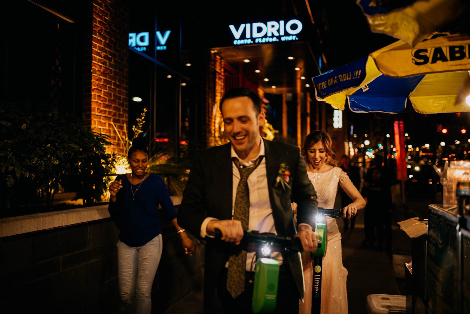 bride and groom ride by a hot dog stand on their Lime scooters after their Vidrio wedding