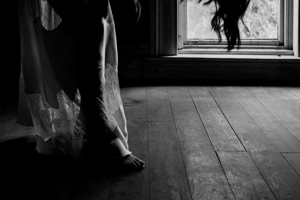 Black and white photo of bride getting into her shoes
