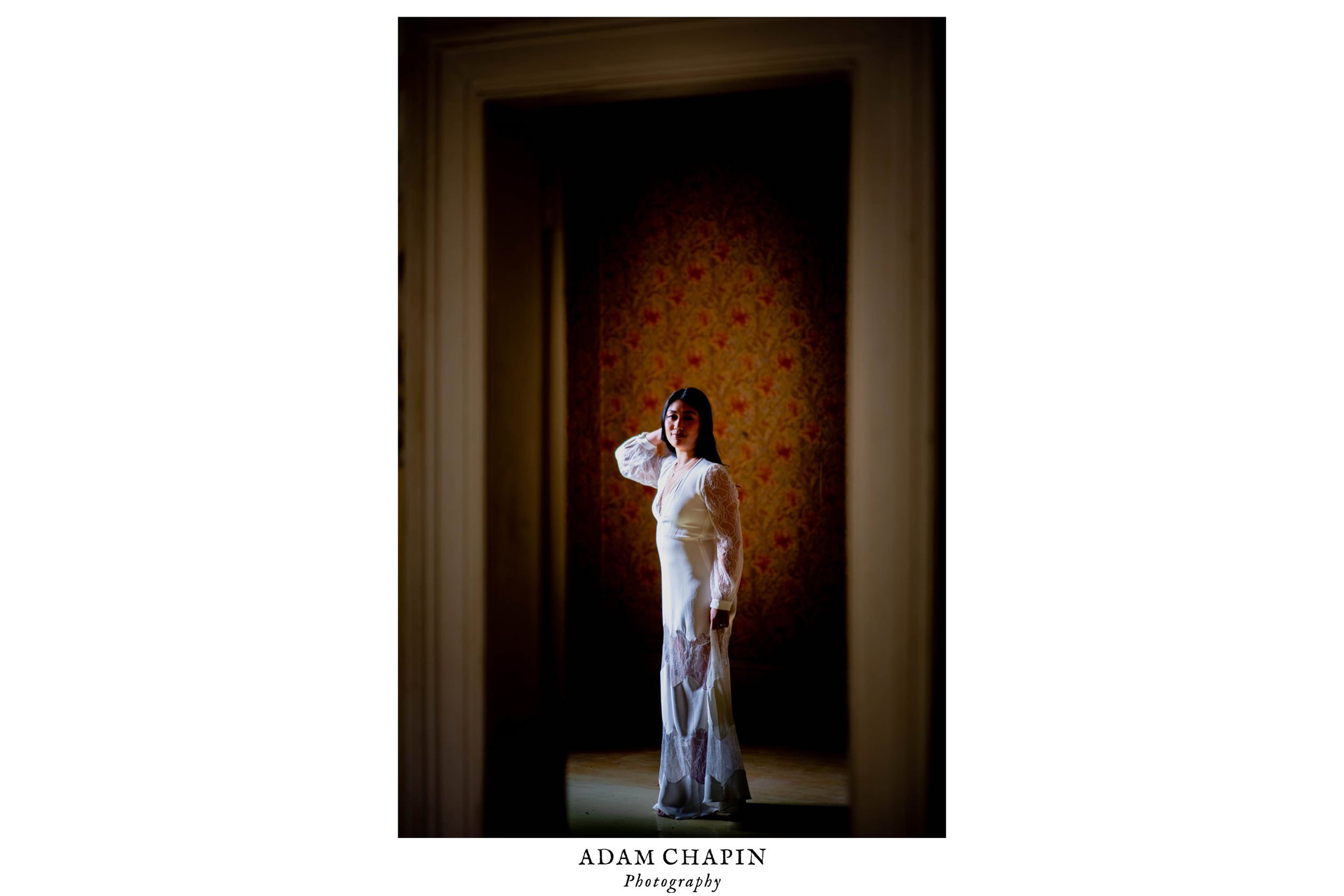 Bride framed by a doorway as she stands in an empty room with ornate wallpaper behind her