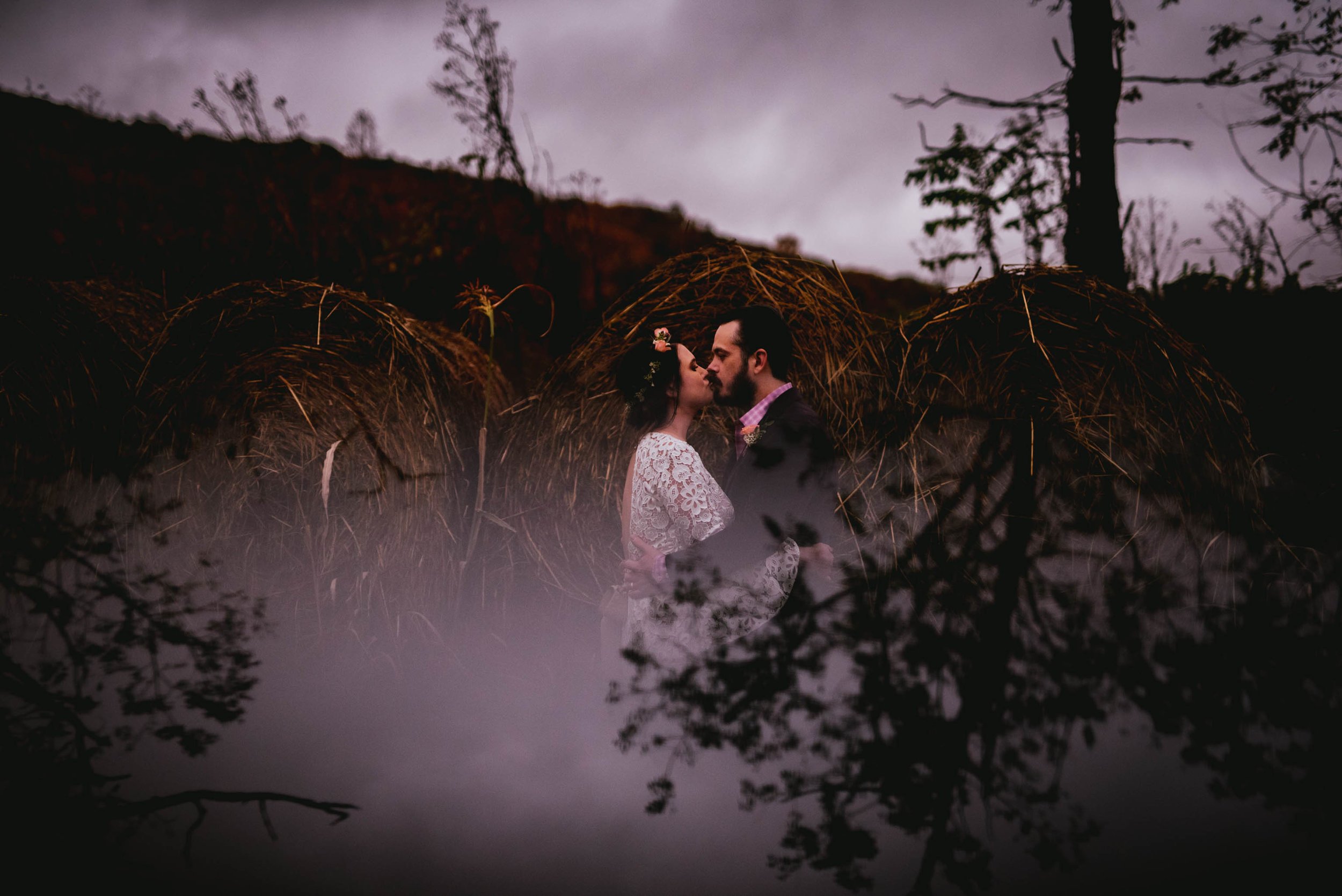 bride and groom kissing in front of the hay bails with the trees reflected beneath them