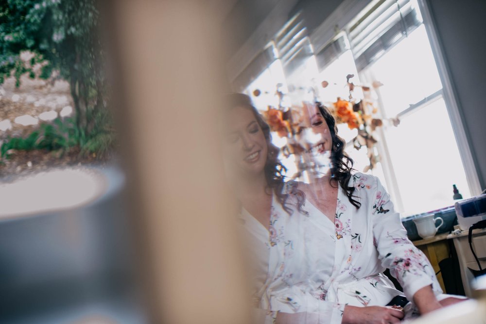 reflection of bride as she finishes up her hair and makeup