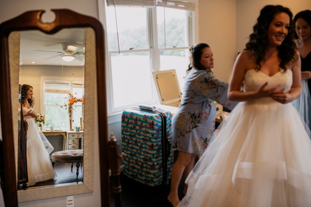 reflection of bride as she finished getting on her dress while her bridesmaids look on