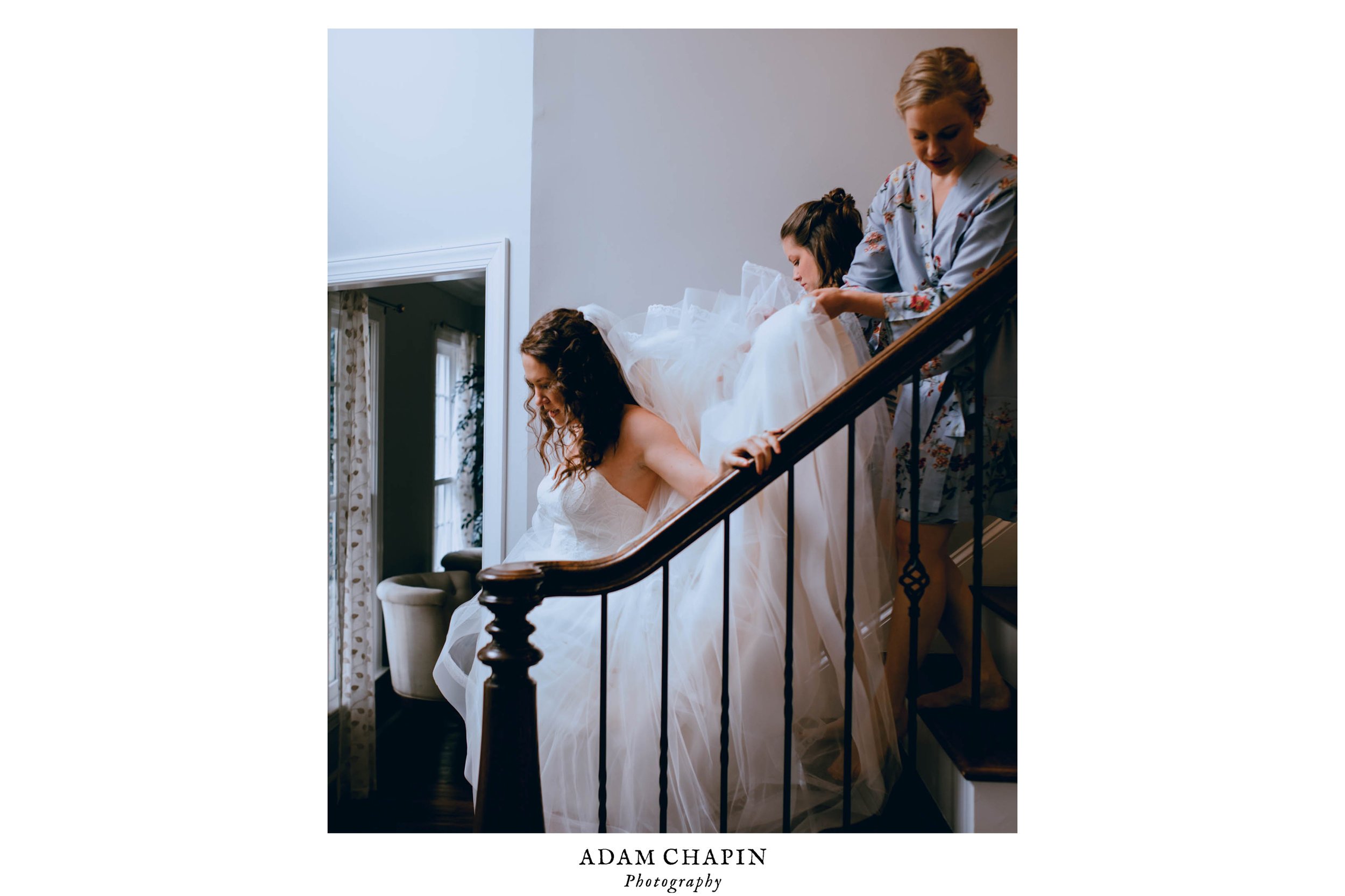 bride coming down the stairs with her bridesmaids carrying her veil and dress