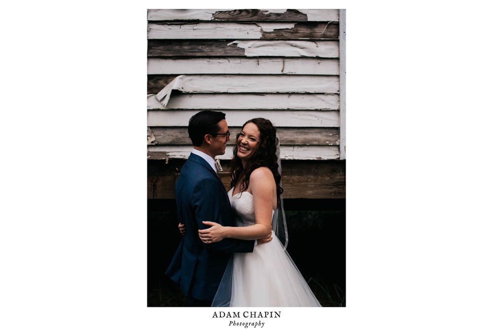 bride and groom laughing with one another in front of a dilapidated house before their wedding ceremony