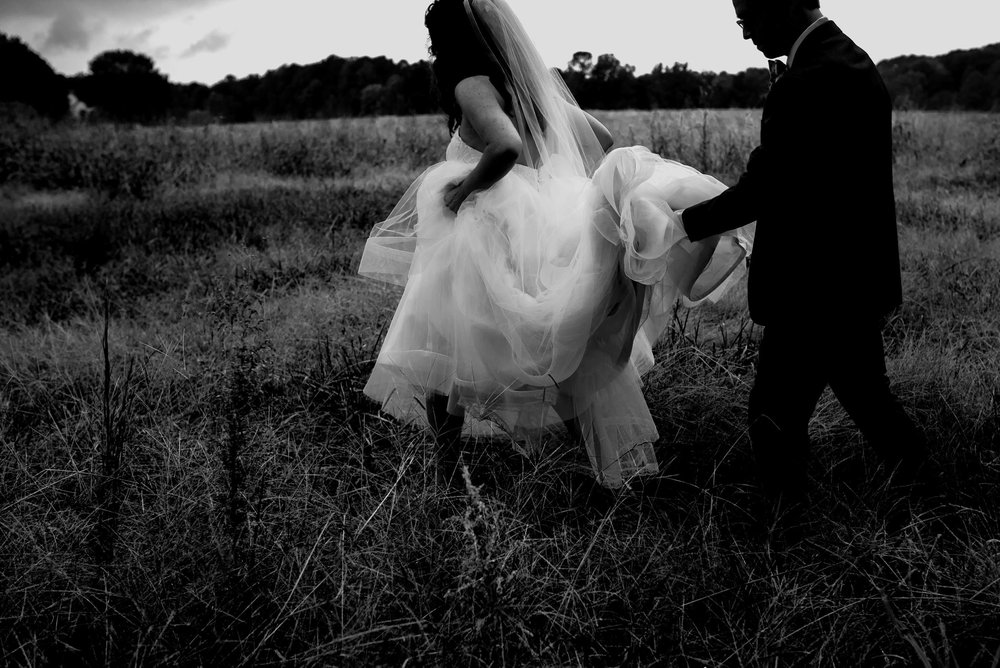 black and white photo of bride and groom walking out of the field during their wedding day