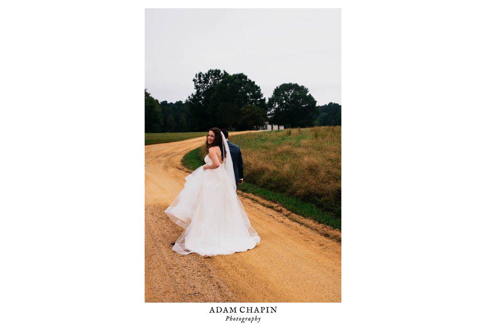 bride and groom walking down the driveway of the Meadows Raleigh as the bride looks back over her shoulder