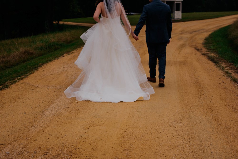 a cropped photo of the bride and groom walking down the drive of their venue to show their hands holding and the details of their wedding attire