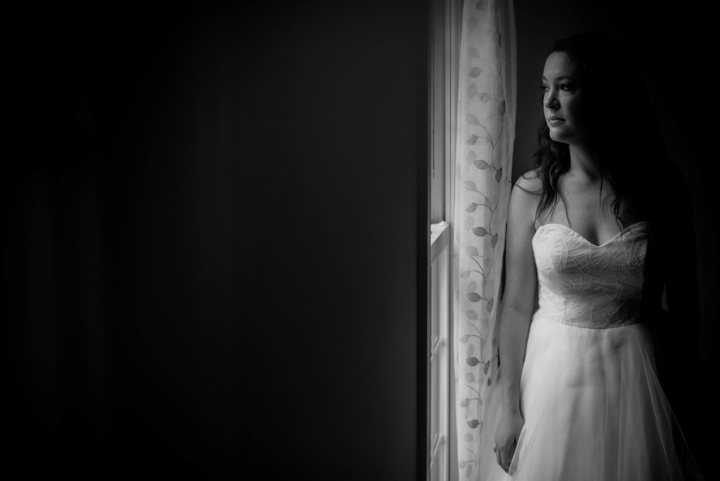 black and white photo of the bride looking out the window before the ceremony