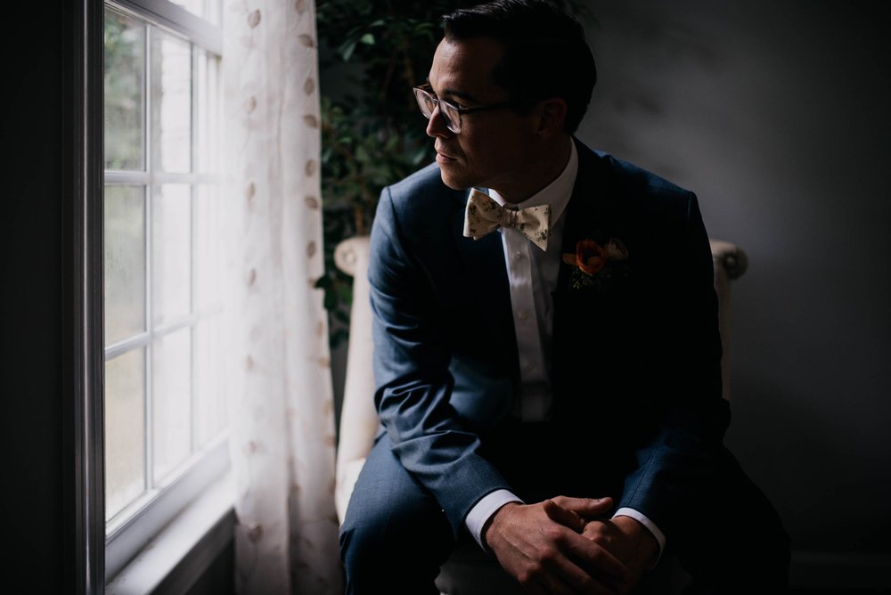 groom sitting in a chair and looking out the window right before the wedding ceremony