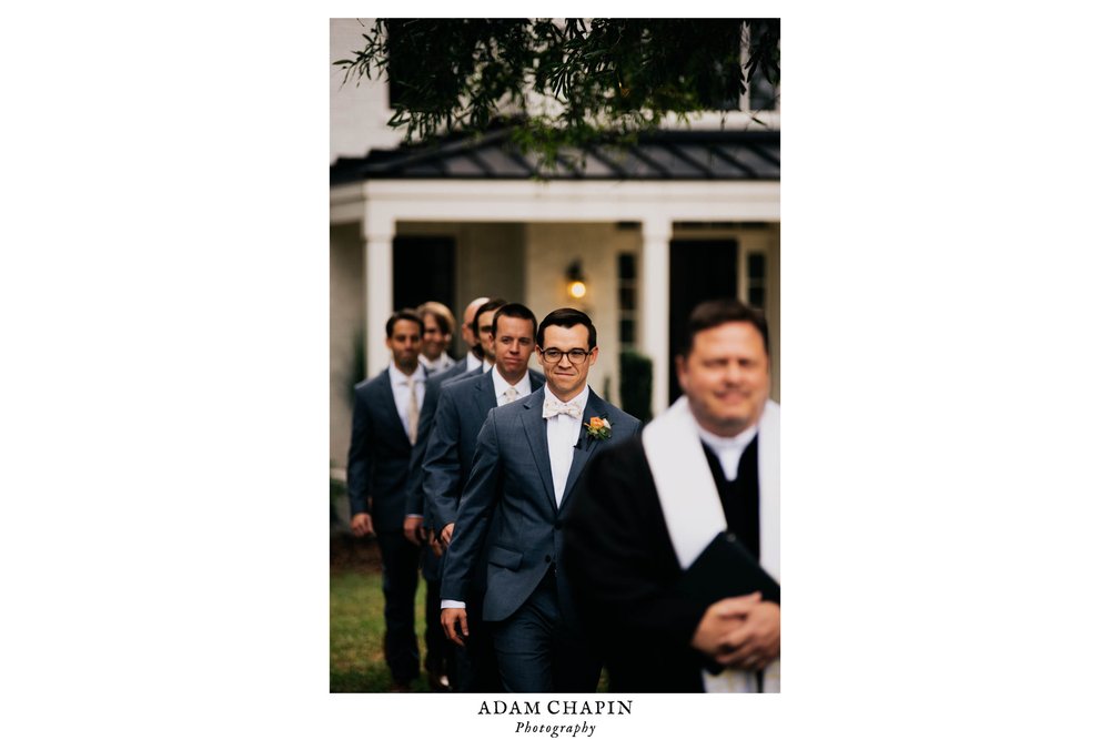 the groom, officiant and groomsmen walk down the aisle at the beginning of the ceremony