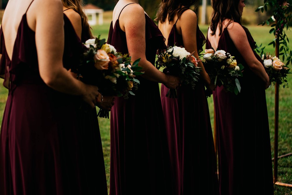 a cropped photo of the bridesmaids dresses and their florals during the wedding ceremony