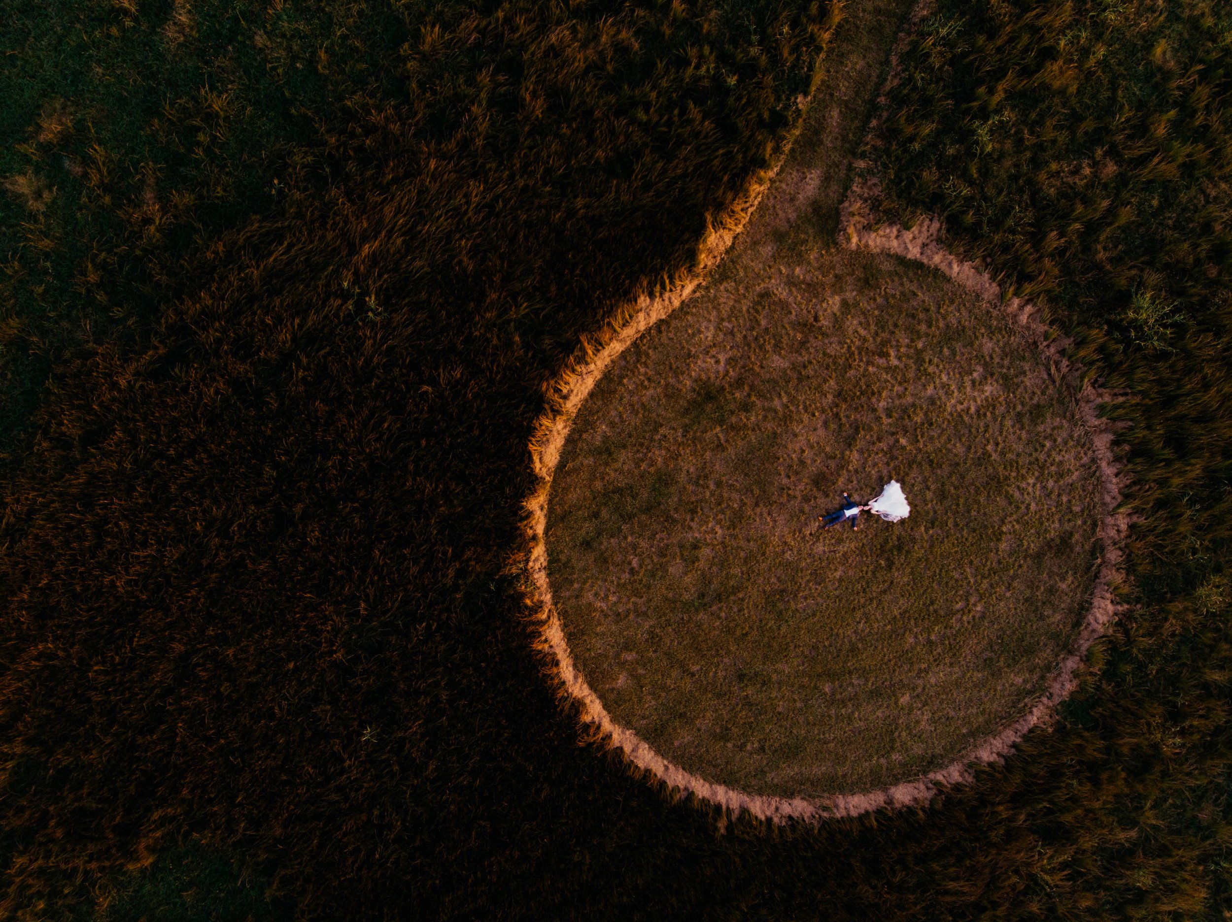 bride and groom laying in a circular cut wheat field during sunset as seen from above