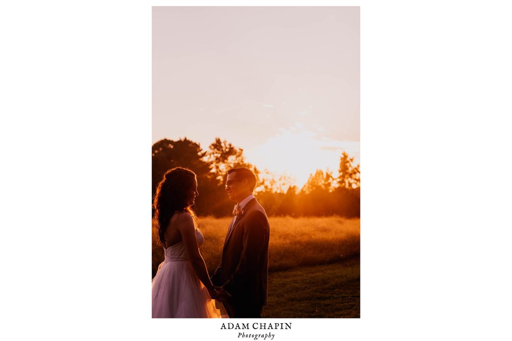 bride and groom standing by a meadow as the sun sets on their wedding day