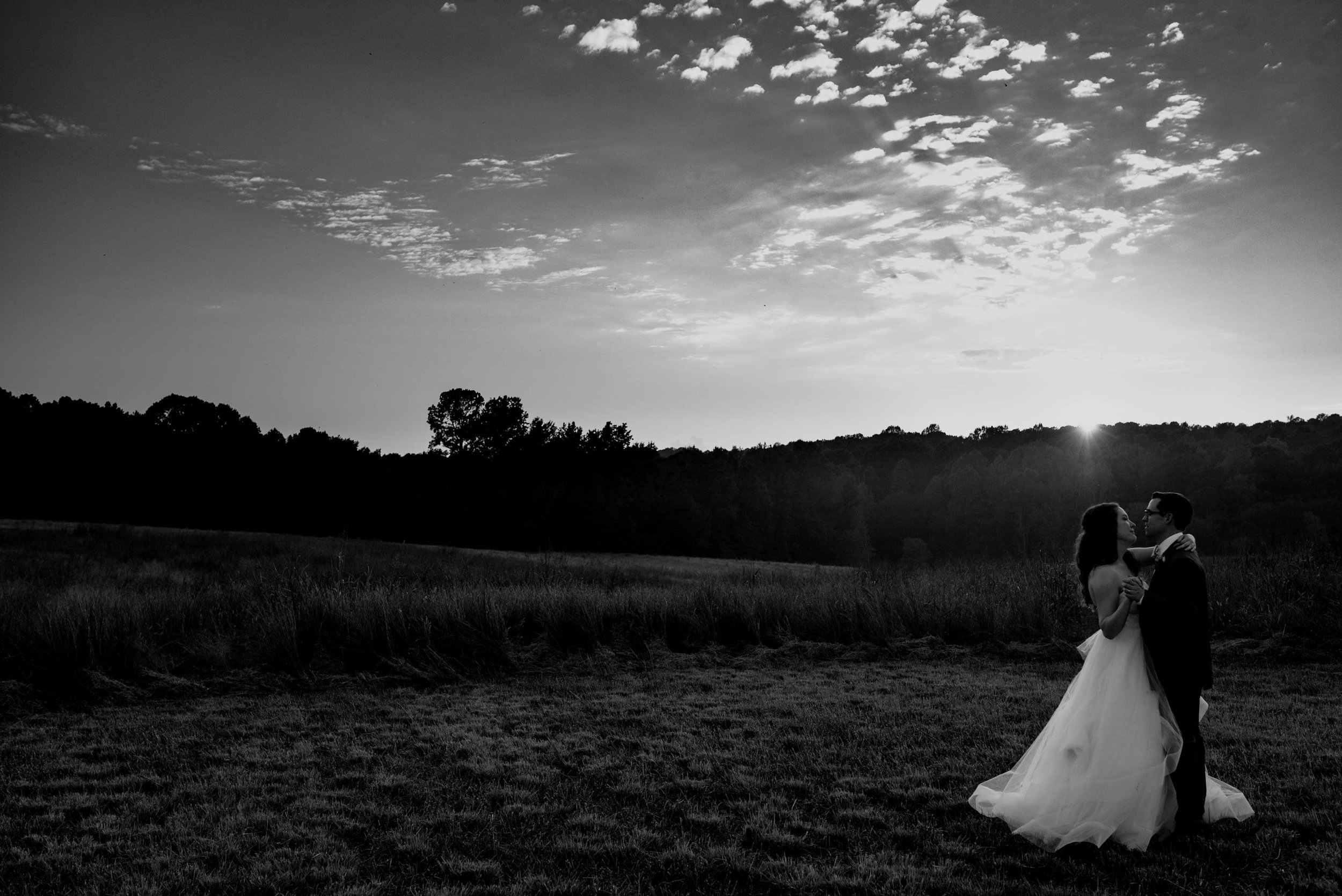 black and white photo of the bride and groom dancing in the sunset in a field during their wedding