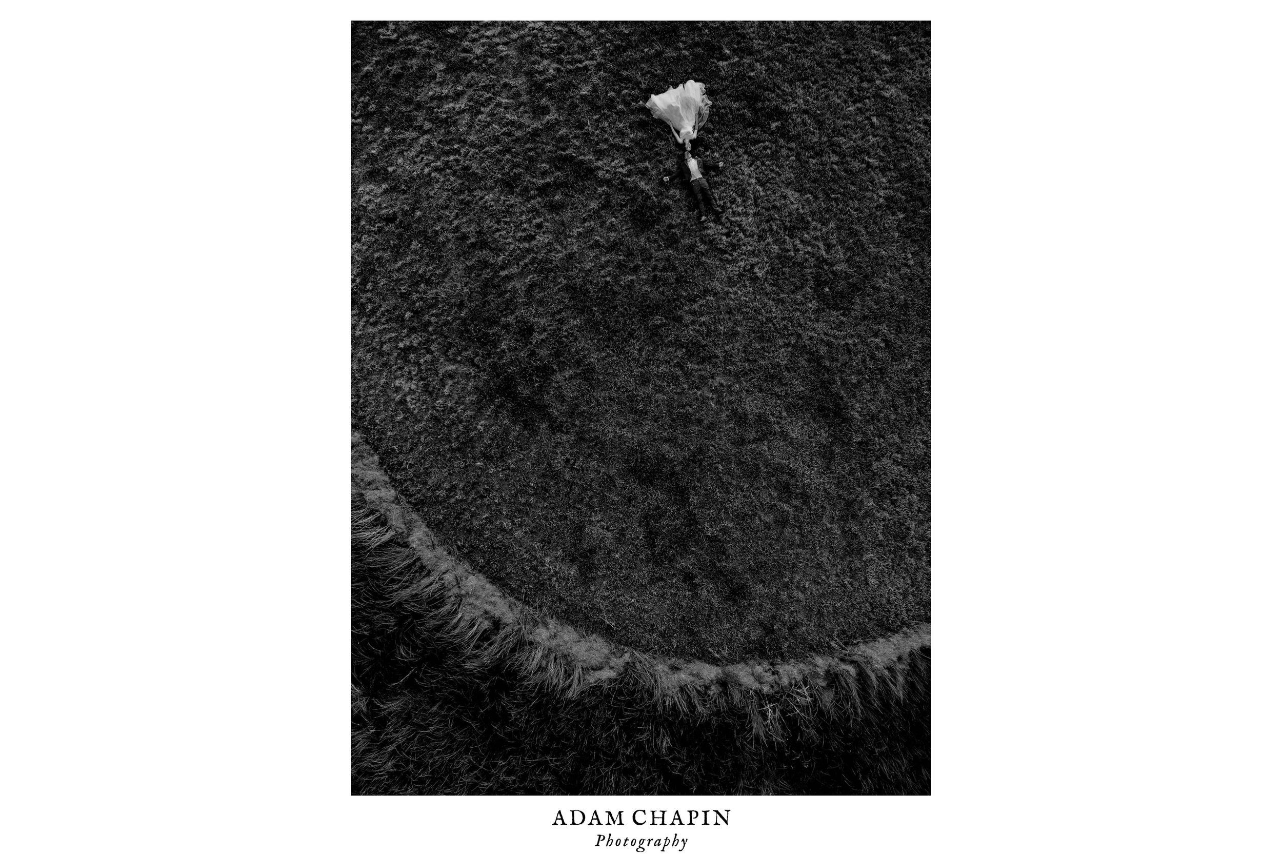black and white drone photo of bride and groom laying down in a circular wheat field