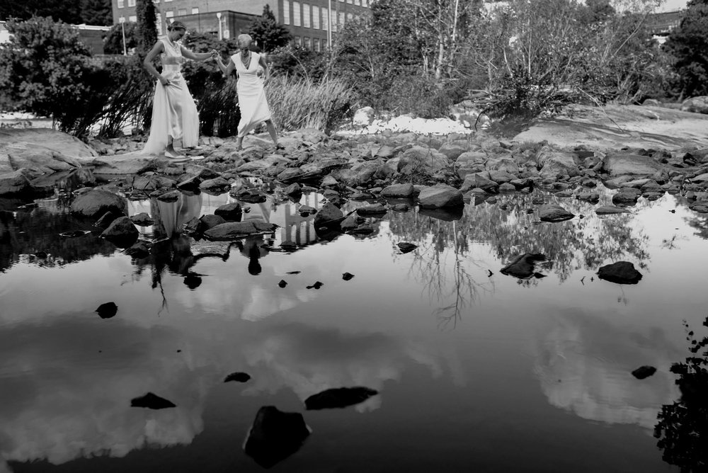 brides walking across the rocks in the Haw River in saxapahaw north carolina