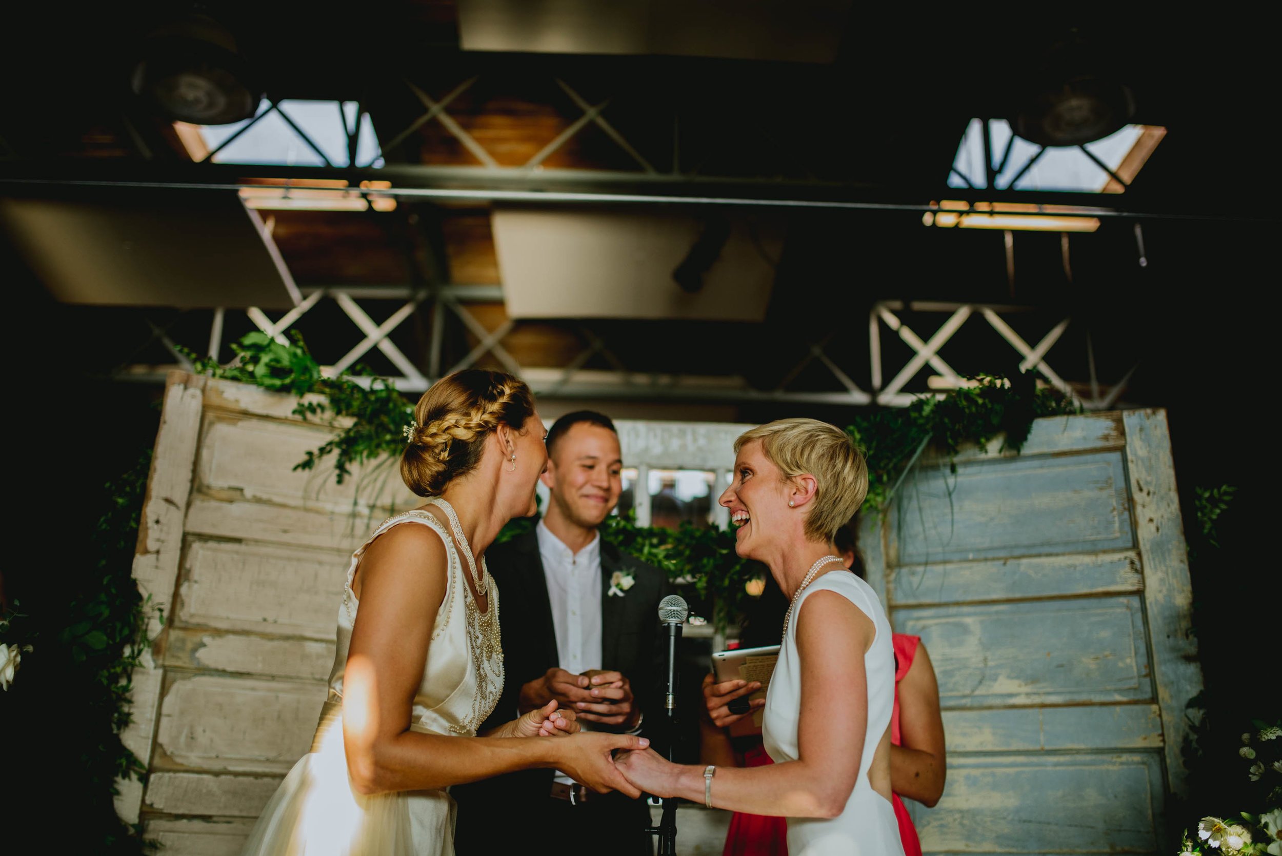 brides share a laugh with their officiants during their haw river ballroom wedding