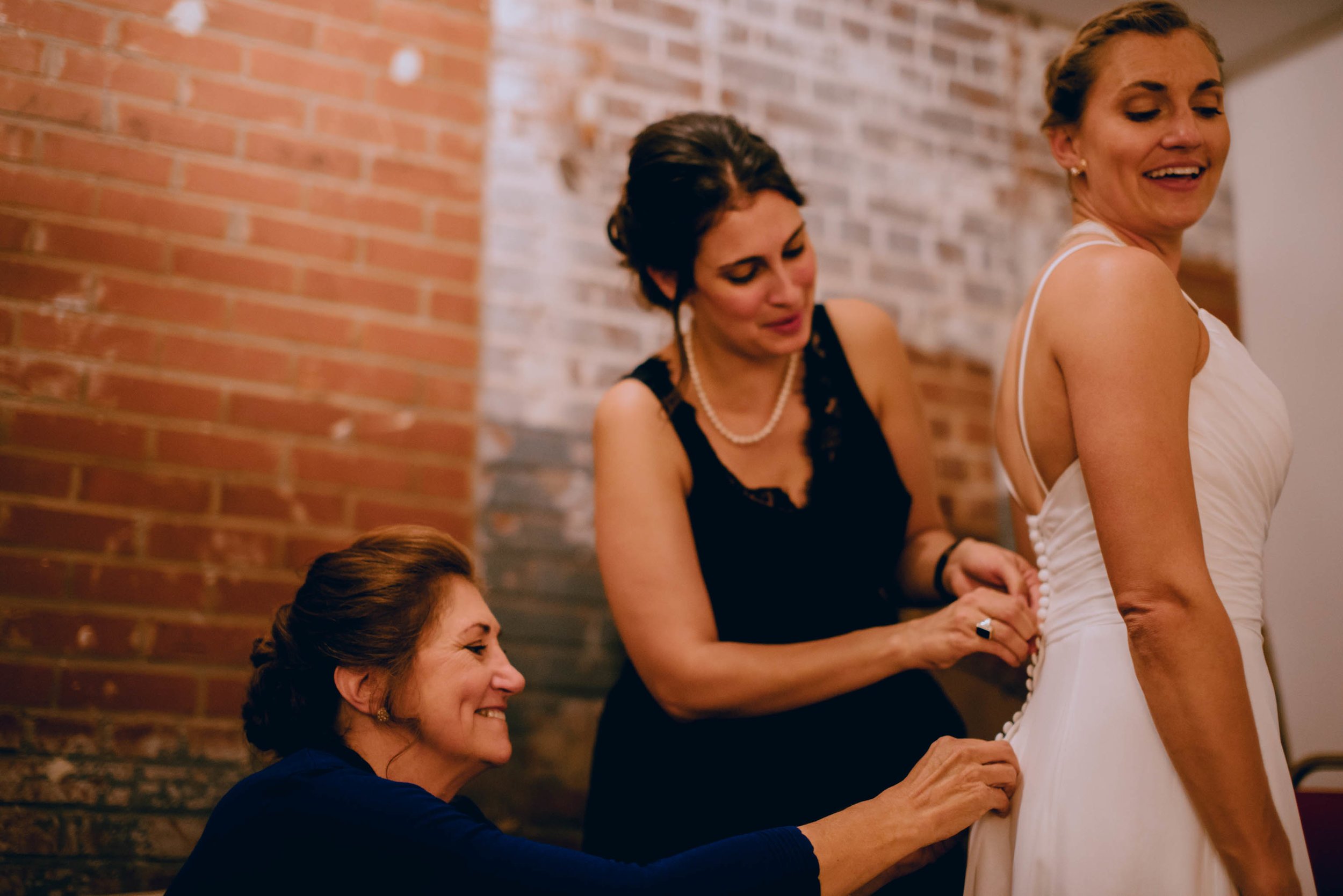 bride changing into her second dress with help of her sister and mother during haw river ballroom
