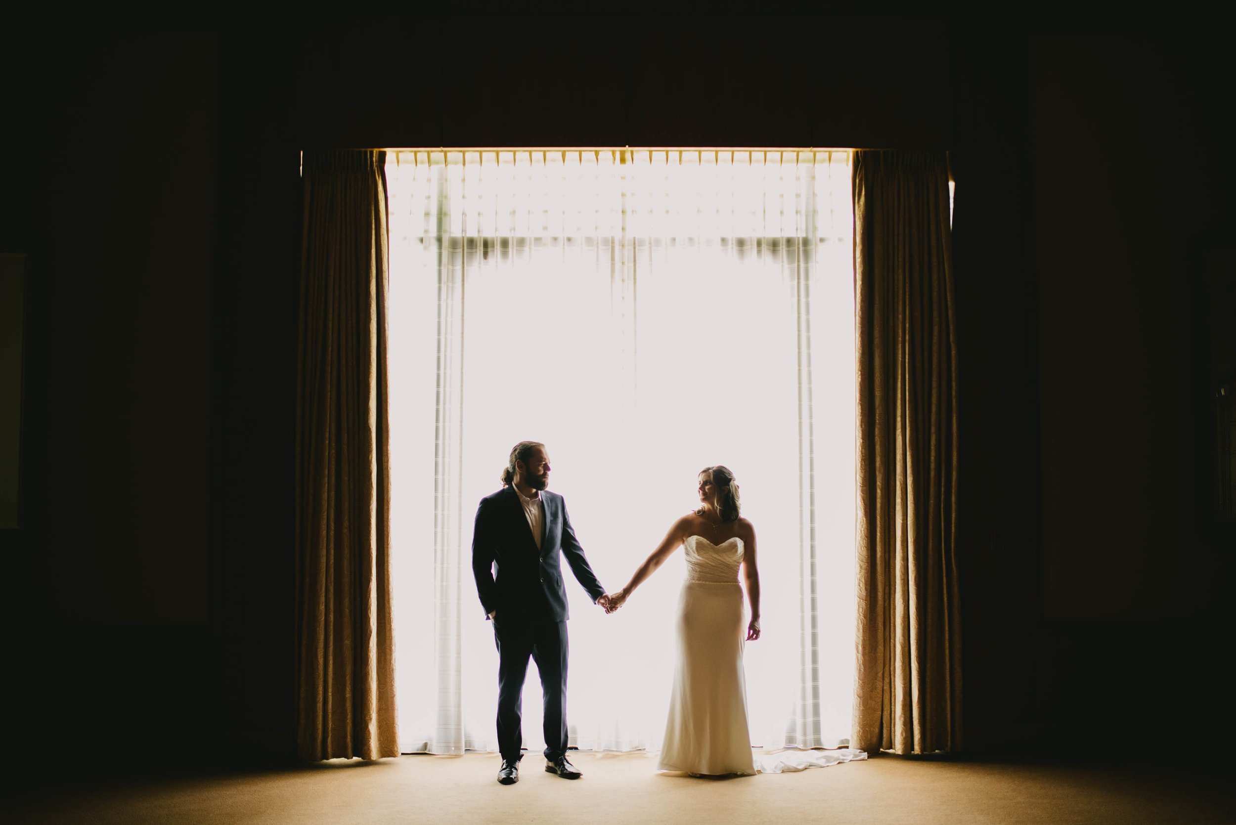 bride and groom holding hands in front of large window at Umstead Hotel and Spa