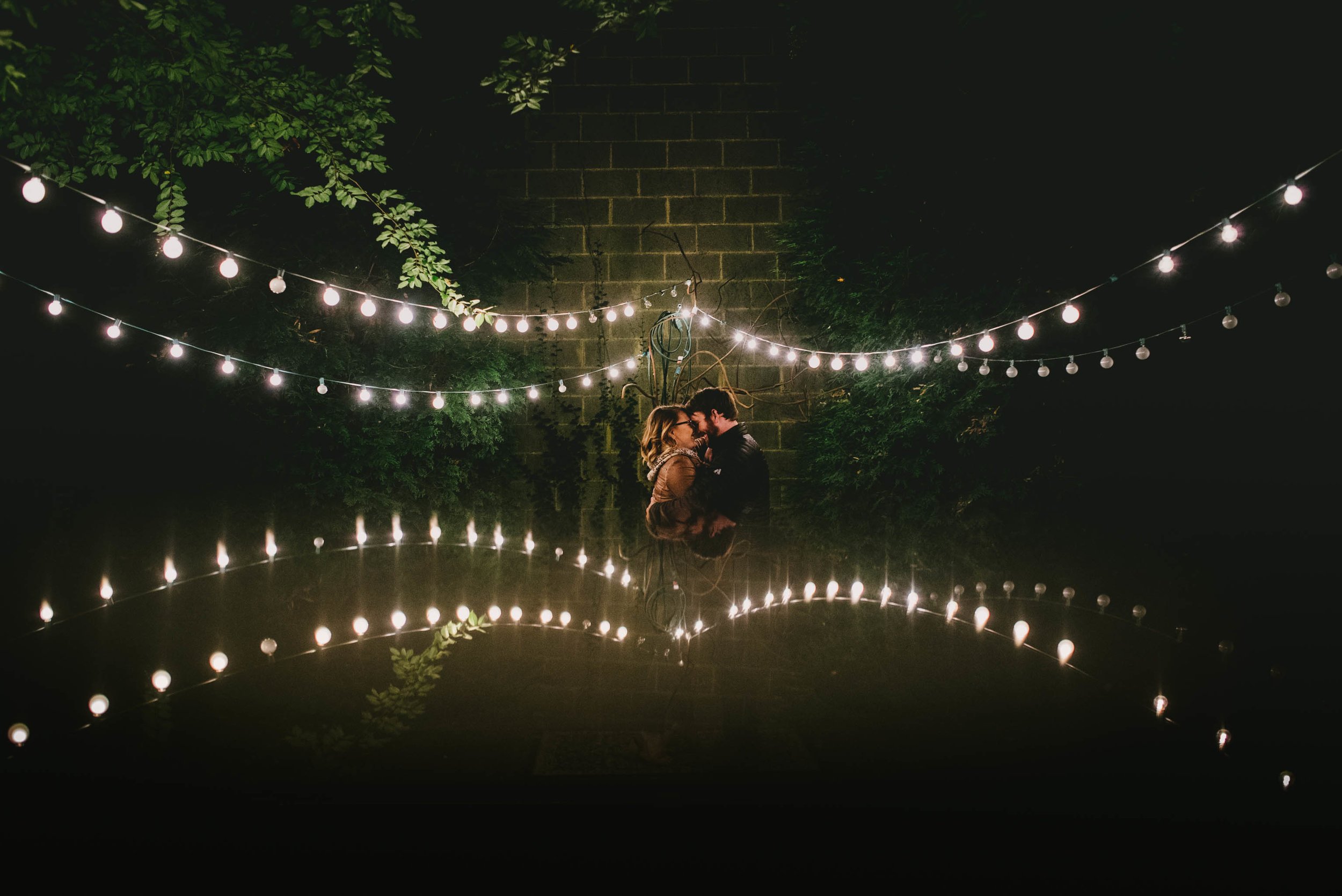 Couple getting close during their engagement photos at the Lindley Park Filling Station under a reflection of the garden tea lights