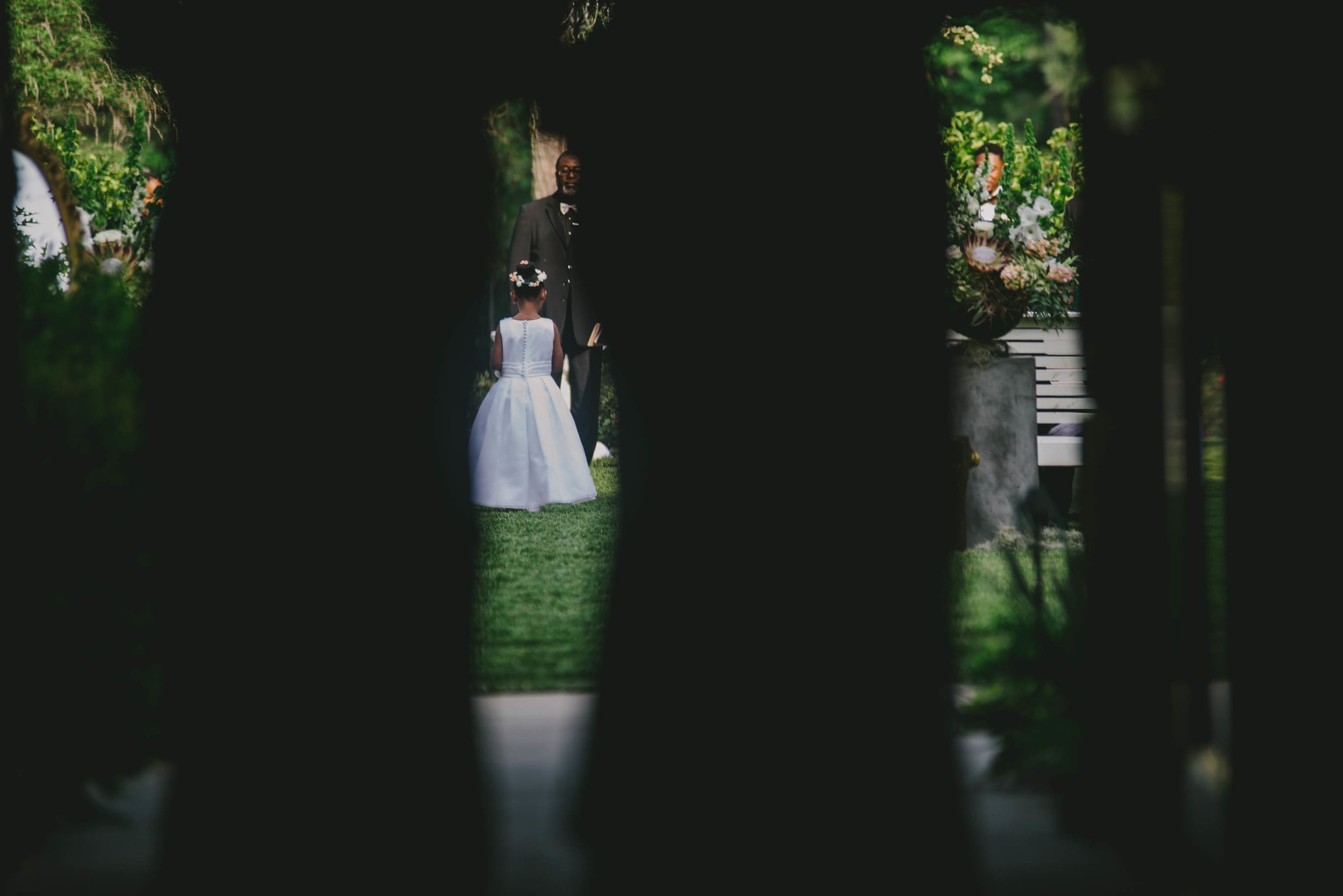 A flower girl as seen between the shadows of the two grandmothers during the processional of the wedding