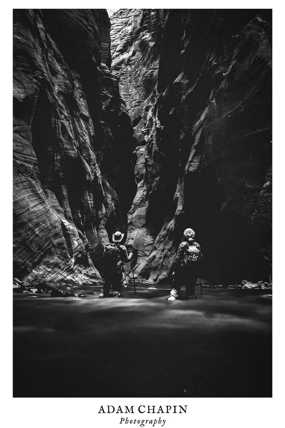 a couple stands in the Virgin river looking down the canyon of The Narrows in Zion National Park