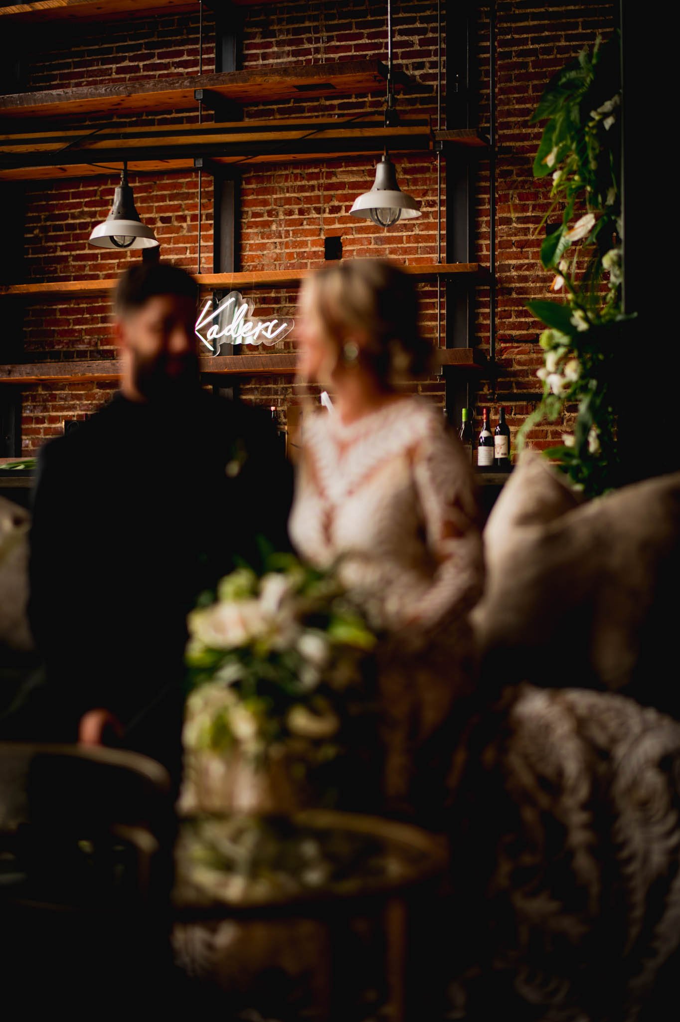 bride and groom talk while their custom neon sign hangs in the background