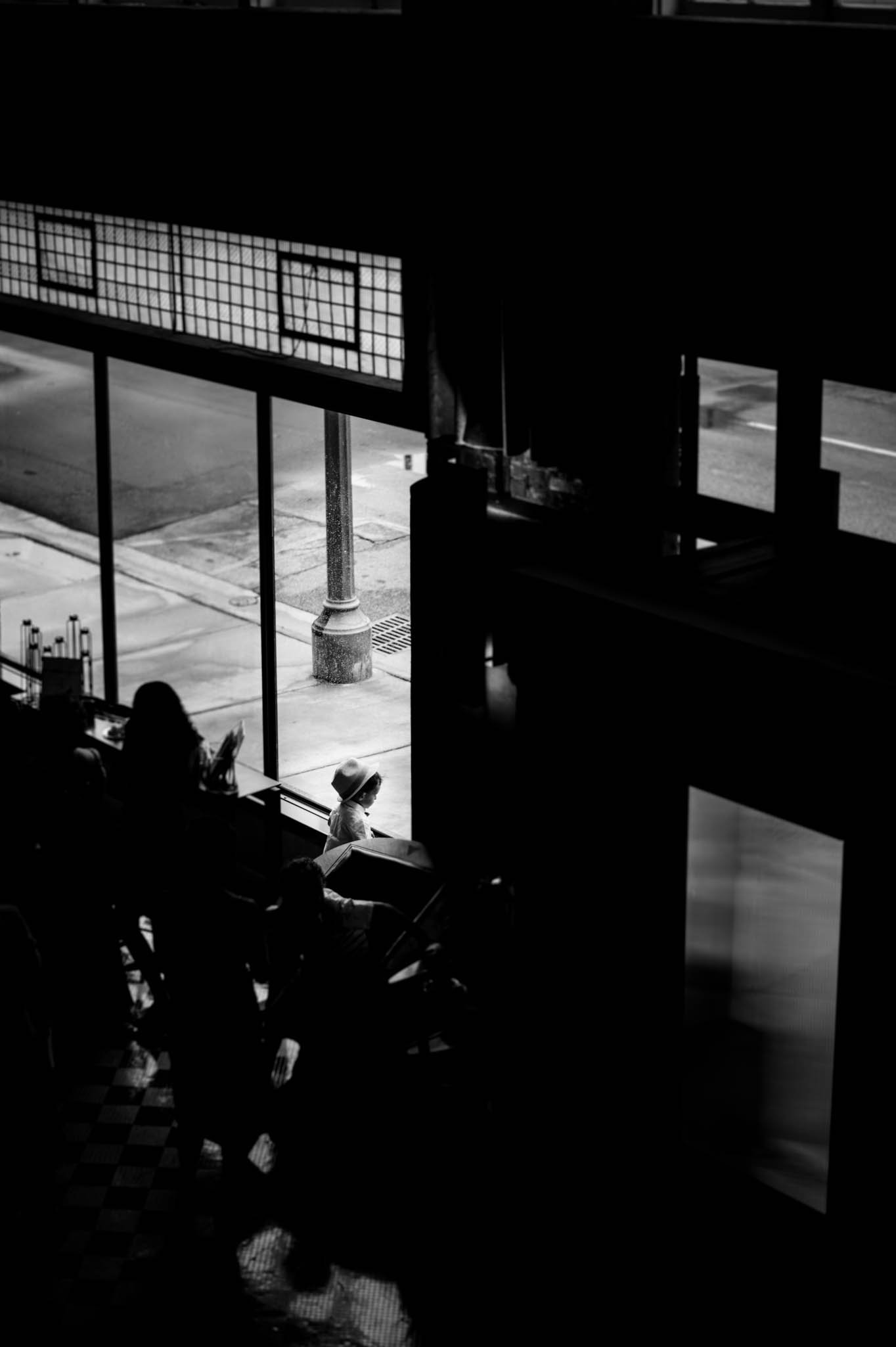 little boy with fedora looks out window during wedding cocktail hour