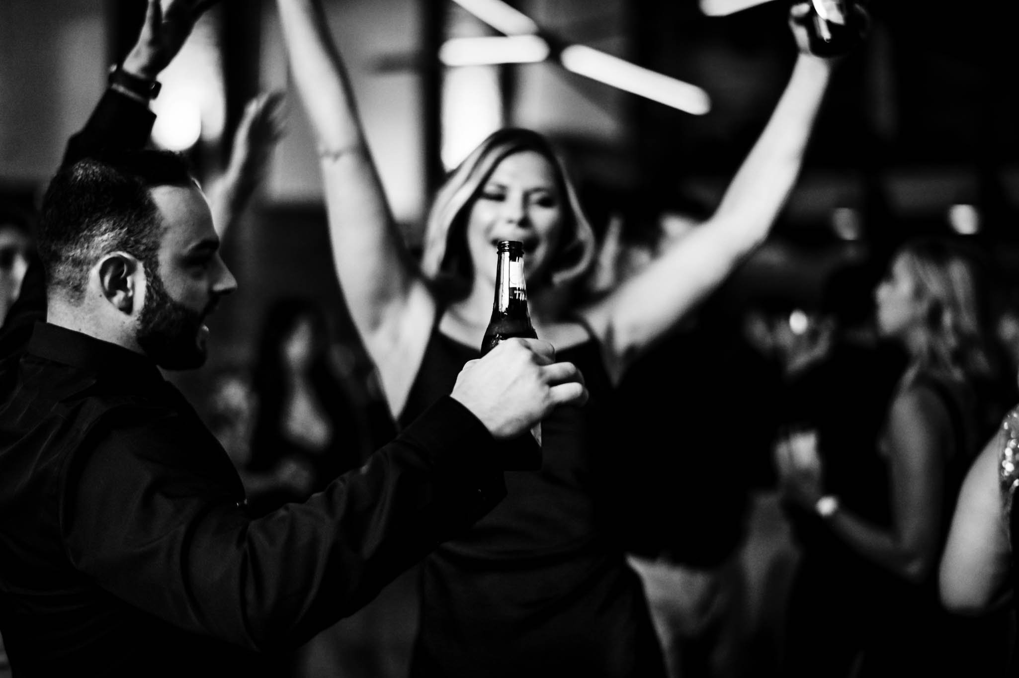 wedding guests sings as a beer bottle is lifted to cover her mouth