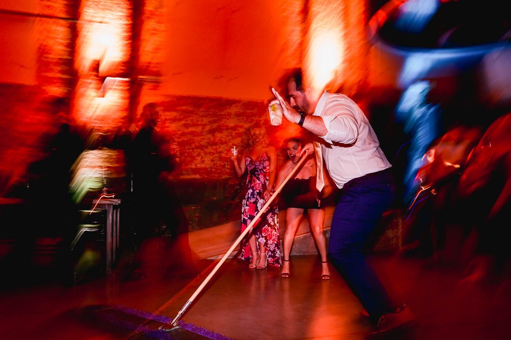 wedding guest sweeps up the floor of broken glass during the reception