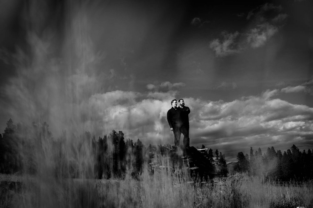 couple stand on a pile of wood at an old mill in colorado