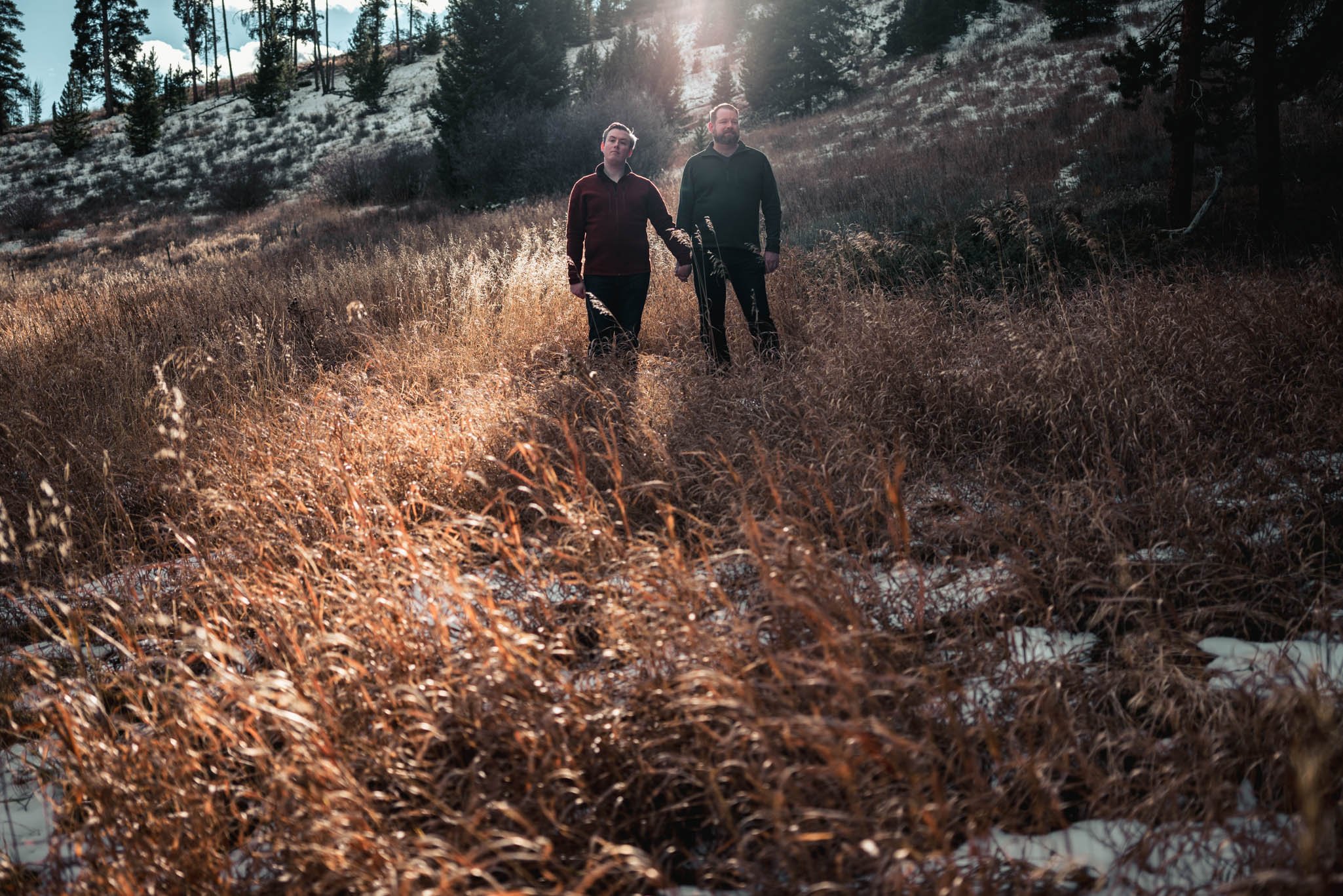couple stand in a field as sun lights them from behind