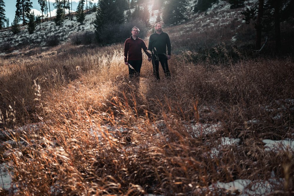 couple stand in a field as sun lights them from behind