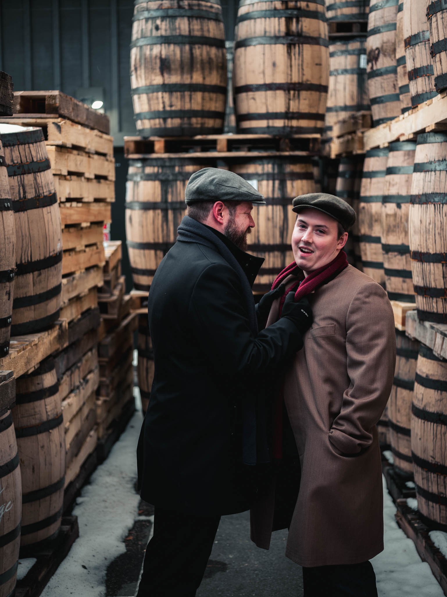 man pulls in his partner while standing surrounded by  whiskey barrels