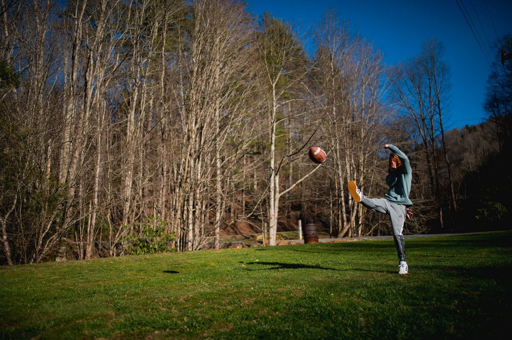 boy punting a football in the backyard