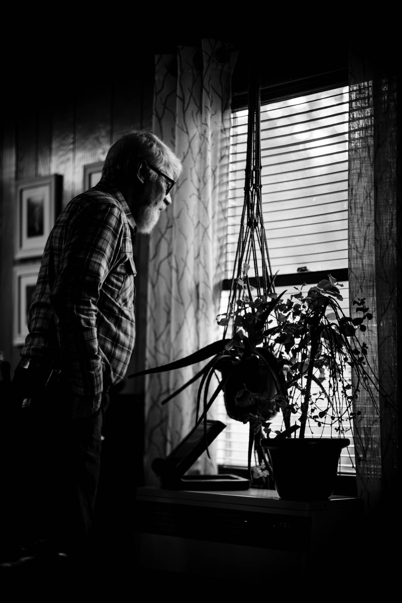 older man looking at his plant by the window