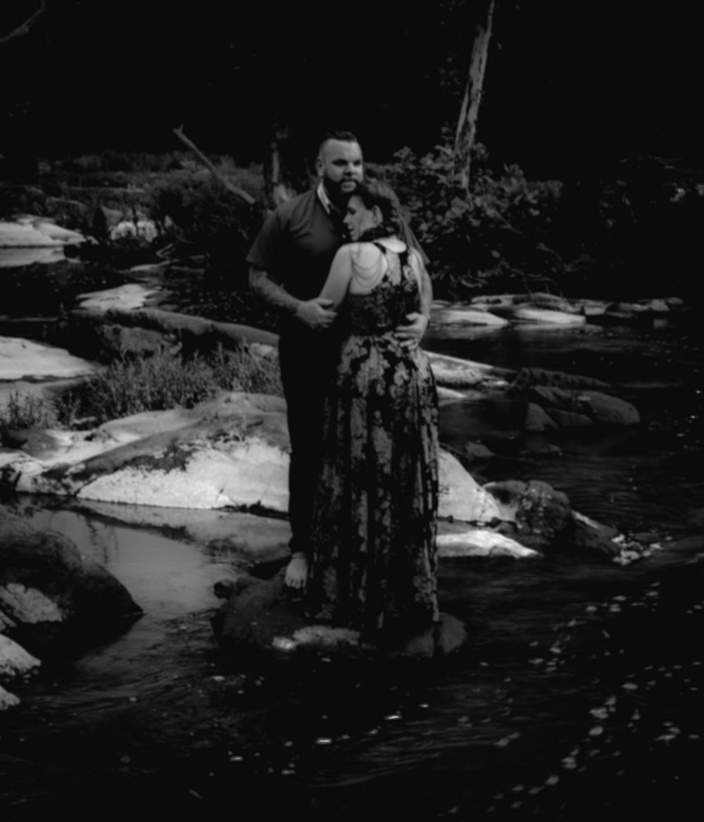 couple hug while standing on a rock on a river