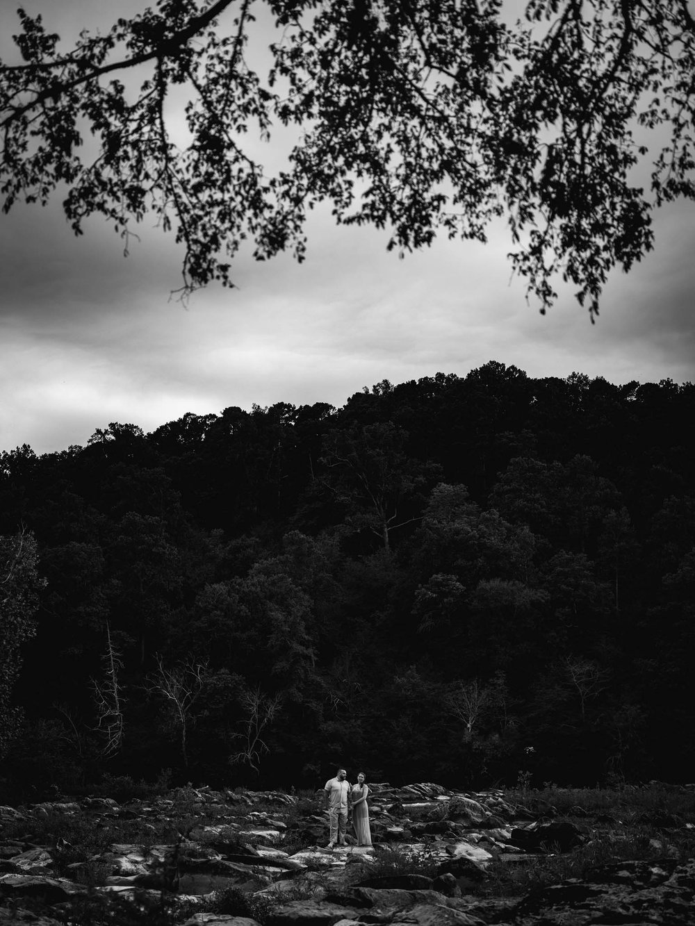 couple stands in the twilight while sitting on the boulders in the river