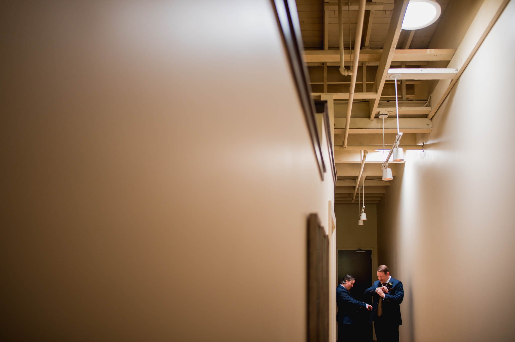 two grooms put on their new cufflinks in a hallway
