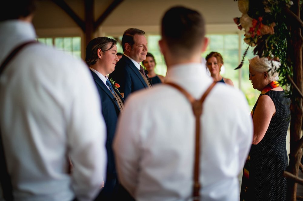 two grooms stand before the officiant of their wedding during the ceremony