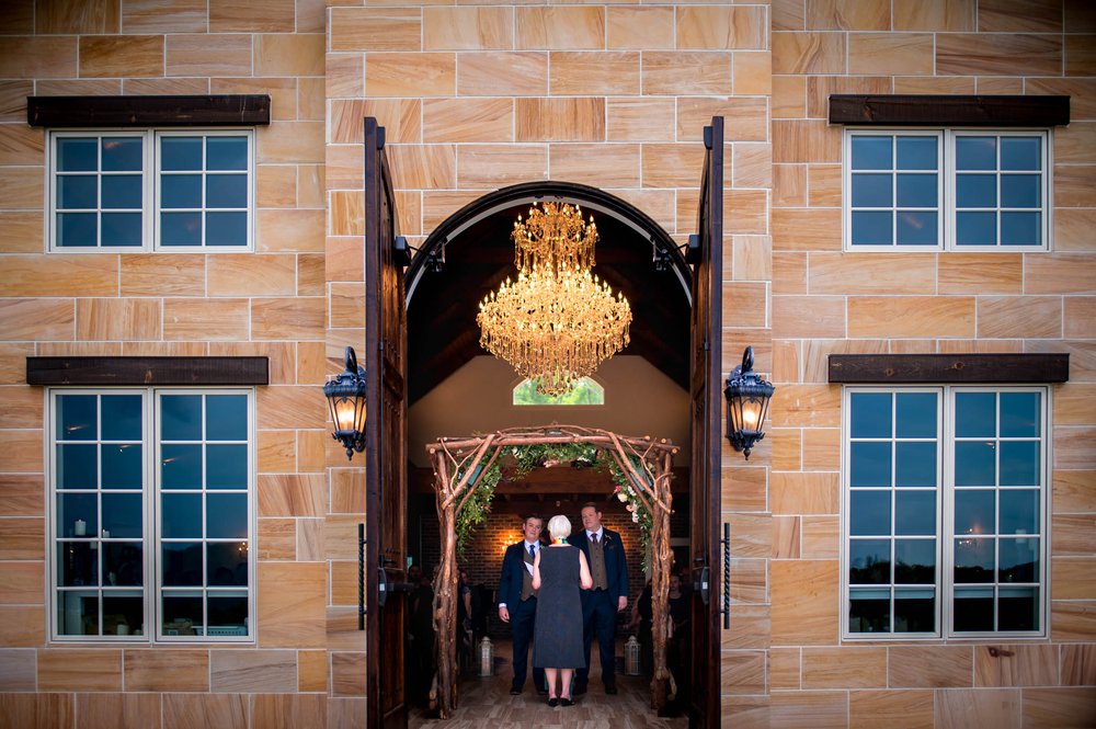 two grooms seen through the large doors of the Ridge wedding venue during their ceremony