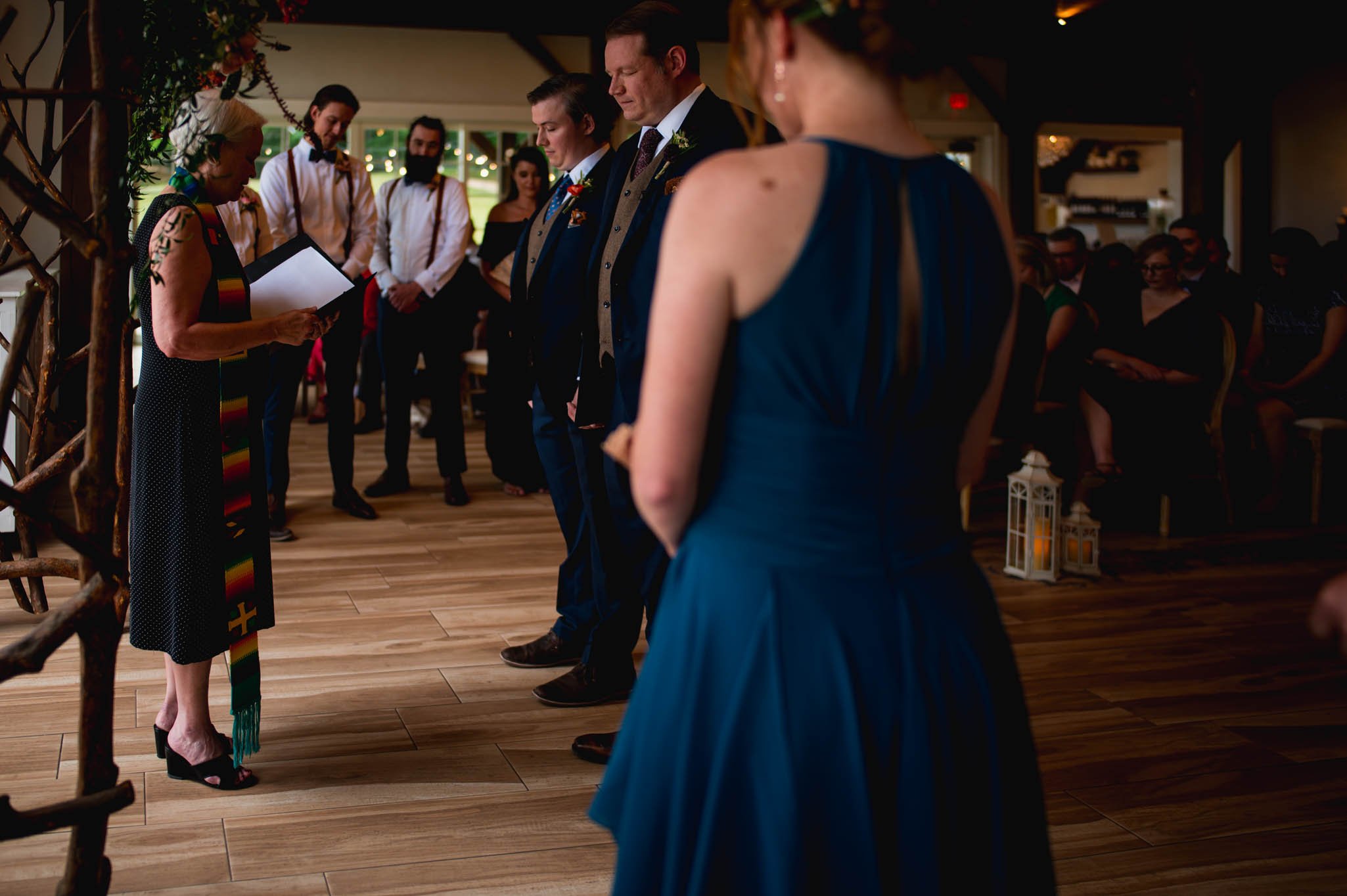 two grooms stand for their wedding ceremony and surrounded by family and friends